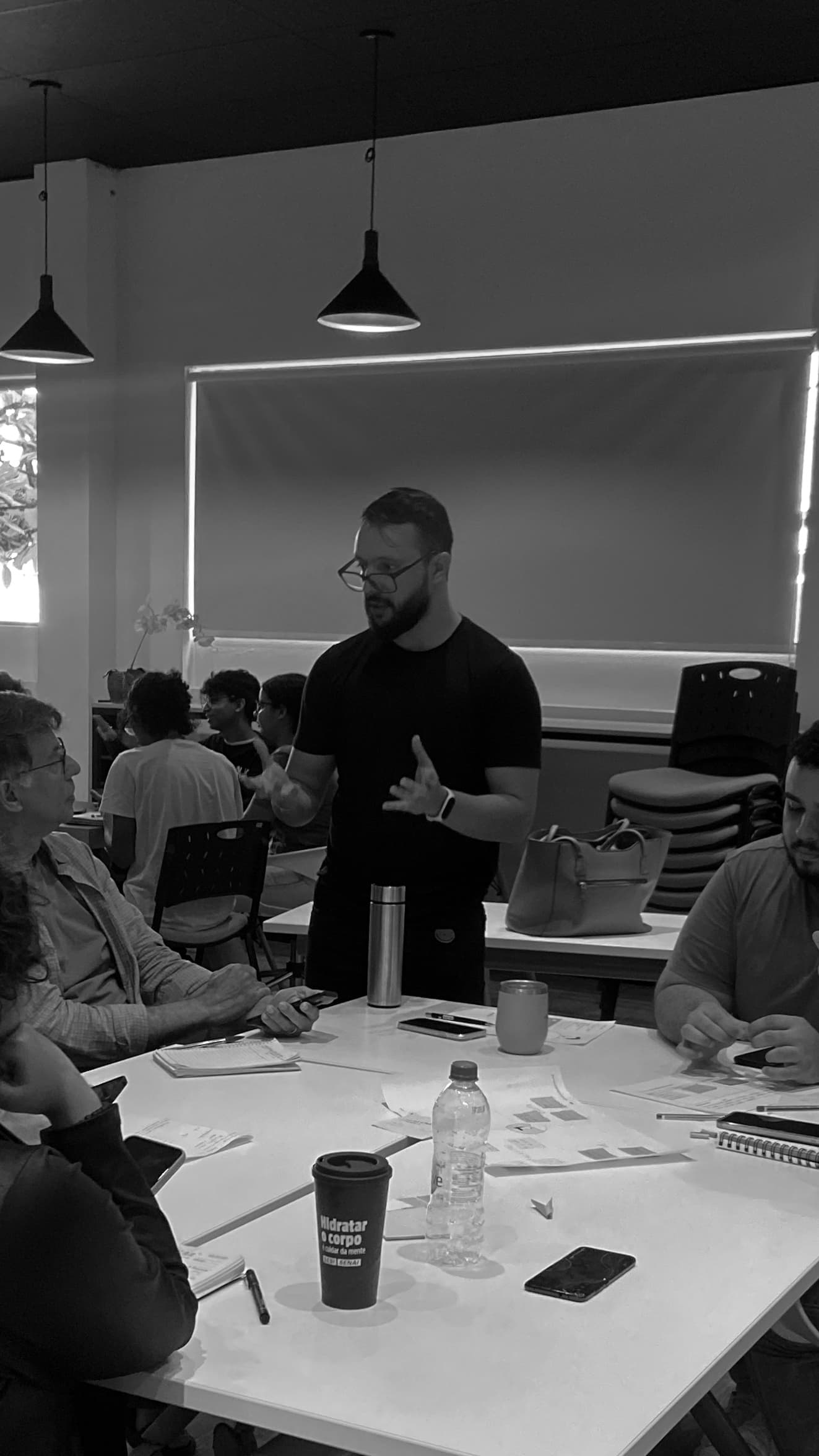 João Paulo em pé, conversando com um grupo sentado ao redor de uma mesa